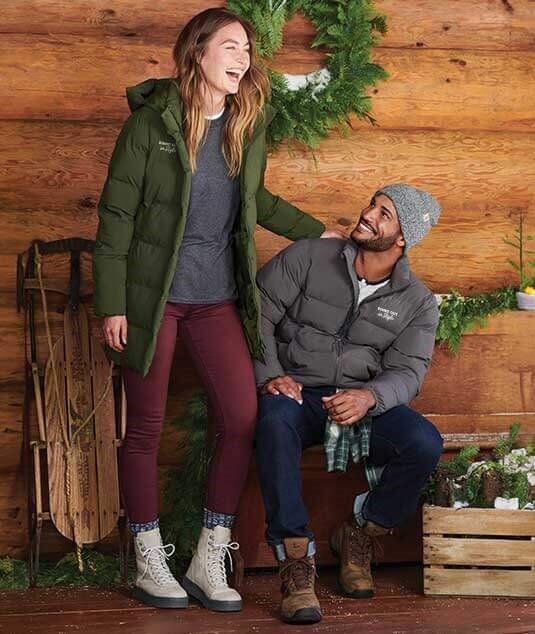 Two happy people wearing custom printed jackets and beanies in a festively decorated cabin.