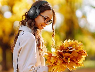 Person wearing headphones walking outside with fall leaves.