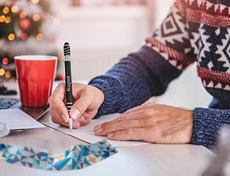 Person sitting at a table, in a holiday sweater, using a branded pen.