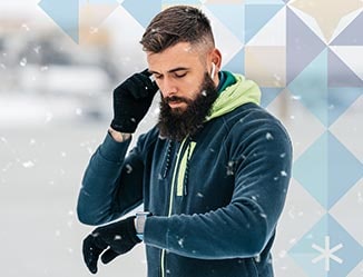 Person wearing headphones standing outside in the snow looking at a smart watch.